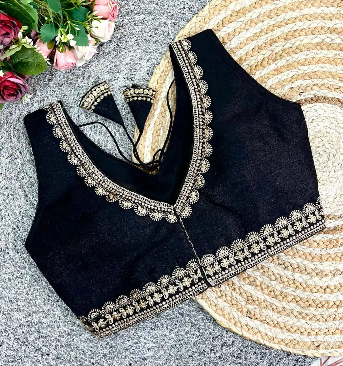 Black blouse with intricate gold embroidery on a textured surface with flowers and a fan.